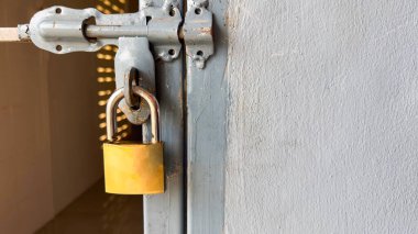 Kalıplı gri metal bir kapının üzerinde parlak altın bir kilit. Güvenliği, korunmayı ve güvenilirliği simgeliyor. Anahtarın zarafeti ve engebeli kapı yüzeyi arasında bir tezat oluşturuyor.