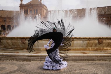 Female flamenco dancer, teenage brunette and beautiful typical Spanish dancer is dancing with a black shawl in front of a fountain in a square in seville. Flamenco concept of world cultural heritage.