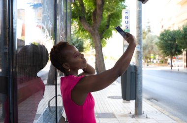 Otobüste oturan genç ve güzel Afro-Amerikan kadın cep telefonuna danışmayı ve otobüs beklerken kendi fotoğrafını çekmeyi bırak. Toplu taşıma kavramı