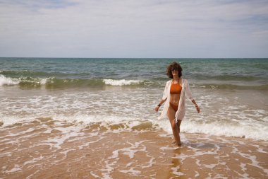 Sahilde yürüyen bikinili güzel bir kadın. Kadın farklı jestler ve ifadeler yaparken bir cennet kumsalına yolculuğunun tadını çıkarıyor..
