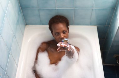 Genç ve güzel Afro-Amerikan kadın küvette köpük banyosu yapıyor. Güzellik ve hijyen kavramı.