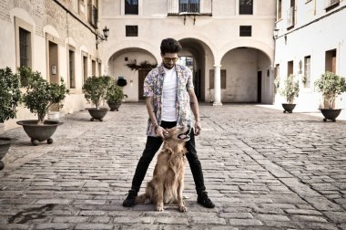 young latin man and his brown golden retriever dog, the man standing up looks at his pet who is sitting on the ground and grabs his head. Pets concept.