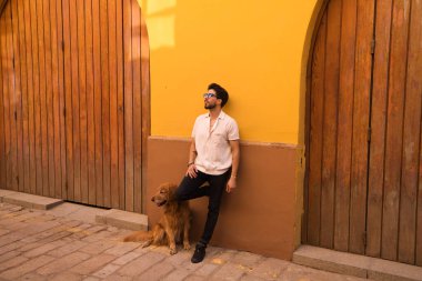 young latin man and his brown golden retriever dog, the man standing up looks at his pet who is sitting on the ground and grabs his head. Pets concept.