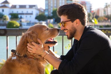 young latino man with sunglasses and beard and his brown golden retriever dog look at each other with love and affection. Concept pets, animals, dogs, love to retriever pets.