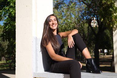 Parkta oturan güzel, koyu renk saçlı İspanyol kadın. Kadın mutlu ve mutlu ve Seville 'de güneşli bir günün tadını çıkarıyor. Kadın siyah giyiyor..