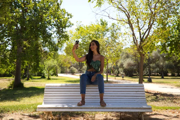 머리를 아름다운 스페인 공원에 벤치에 있습니다 여성은 휴대폰으로 사진을 있습니다 — 스톡 사진