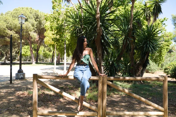 stock image Beautiful woman with black hair leaning on a wooden railing in the park. The woman is doing different body postures while posing for photos. Autumn and nature concept.