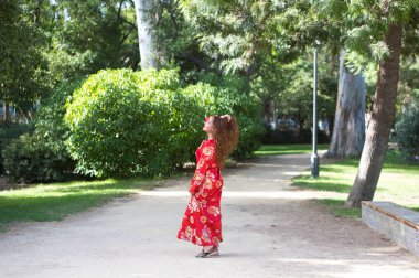 Güzel bir kadın geleneksel bir Fas elbisesi giyer. Kırmızı ve gümüş işlemeli. Kız Fas tarzı bir bahçede, fıskiyeli ve yemyeşil bir yerde düğün fotoğrafları için poz veriyor..