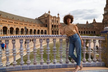 Kıvırcık saçlı güzel kadın Sevilla 'da tatilde. Kadın, yüzyılın en ünlü meydanının önünde poz veriyor. Tatil ve seyahat kavramı.