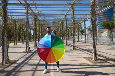 Yakışıklı genç mavi gözlü eşcinsel bir parkta yürüyor ve elinde gökkuşağı renkli bir şemsiye tutuyor. Adam çok mutlu. Haklar, homoseksüellik, lezbiyenler.