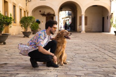 young handsome Hispanic man with his brown golden retriever dog, they are crouched down looking at the same place. Concept pets, animals, dogs, pet love, golden retriever.