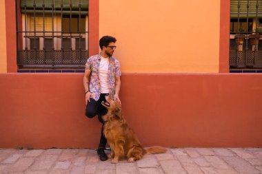 young latin man and his brown golden retriever dog, the man standing up looks at his pet who is sitting on the ground and grabs his head. Pets concept.