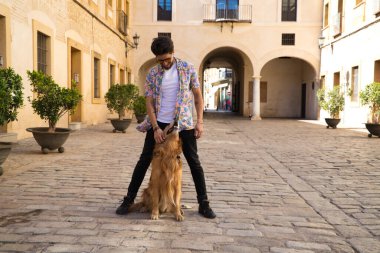 young latin man and his brown golden retriever dog, the man standing up looks at his pet who is sitting on the ground and grabs his head. Pets concept.