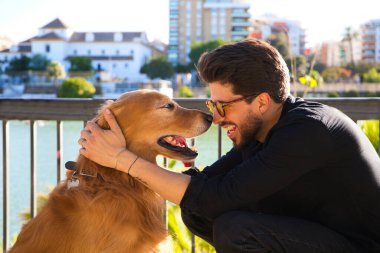 young latino man with sunglasses and beard and his brown golden retriever dog look at each other with love and affection. Concept pets, animals, dogs, love to retriever pets.