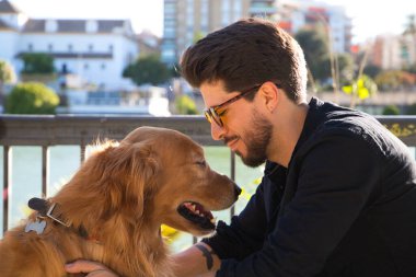 young latino man with sunglasses and beard and his brown golden retriever dog look at each other with love and affection. Concept pets, animals, dogs, love to retriever pets.