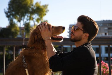 young latino man with sunglasses and beard and his brown golden retriever dog look at each other with love and affection. Concept pets, animals, dogs, love to retriever pets.