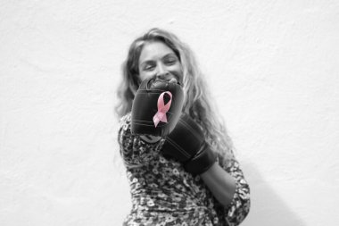 Siyah beyaz kadın portresi, göğüs kanserine karşı pembe kurdeleli boks eldiveni ve beyaz arka planda beyaz bluz giyiyor. Ekim ayı kanser günü.