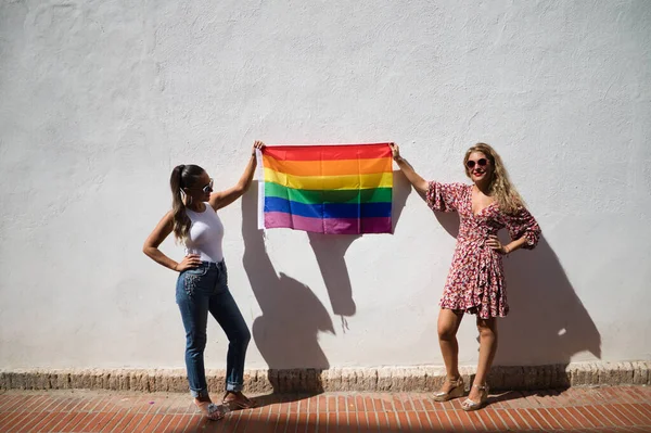 サングラスをかけた2人の若い女性がゲイのプライド旗を手に持っています 女性たちはゲイのプライドの日を喜んでいる 平等概念同性愛Lgtb — ストック写真
