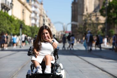 Tekerlekli sandalyedeki genç ve güzel engelli kadın ve hareket kabiliyetinin azalması tatilde olduğu şehirde gezinin keyfini çıkarıyor..