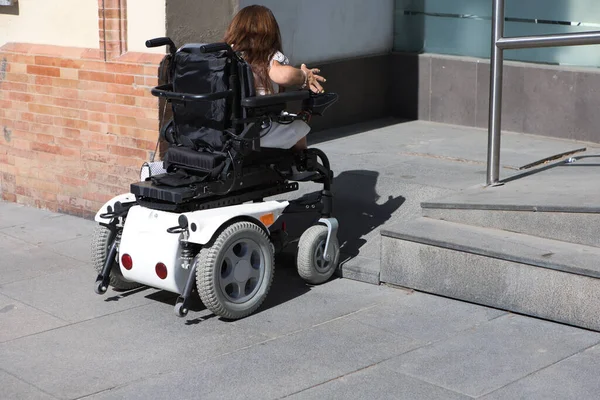 Tekerlekli sandalyede hareket kabiliyeti düşük genç bir kadın tekerlekli sandalye rampasına girmenin önünde bir engelle karşılaşır..