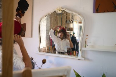 Genç, güzel, girişken bir kadın. Resim ve moda tasarımı sanatına adanmış, kafasına kırmızı bir bere takıyor ve stüdyosunun aynasında kendine bakıyor. Girişimci kadın..