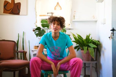 Parlak renkler giymiş genç ve güzel Latin kadın, moda tasarımının sandalyesinde oturuyor ve kameraya poz veriyor ve farklı pozlar ve ifadeler veriyor. kadın gücü