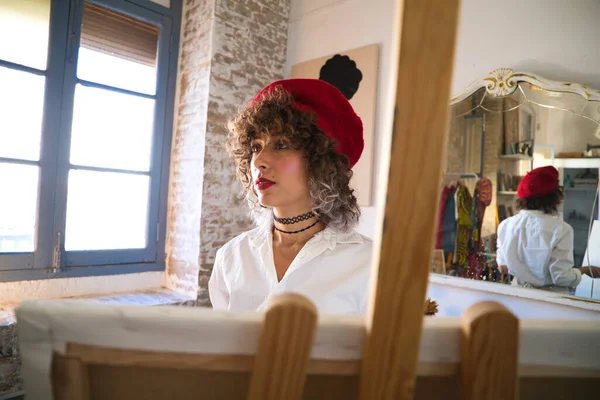 有进取心的女人 她致力于绘画和时装设计的艺术 头上戴着红色贝雷帽 画架上的画布上也画着 创业的妇女概念 — 图库照片