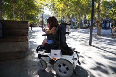 Şehirdeyken akıllı telefon kullanan tekerlekli sandalyedeki güzel ve engelli bir kadın..