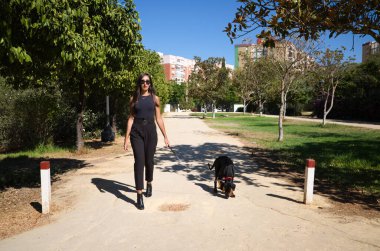 Güzel ve esmer İspanyol kadın bir Doberman köpeği olan köpeğini gezdiriyor. Kadın çok zarif siyah giyinmiş. Evcil hayvanlar ve hayvanlar konsepti.