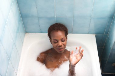 Genç ve güzel Afro-Amerikan kadın küvette köpük banyosu yapıyor. Güzellik ve hijyen kavramı.
