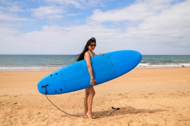 Mavi sörf tahtası olan genç ve güzel bir Latin kadın. Kadın kumsalda. Tatil ve yaz konsepti.