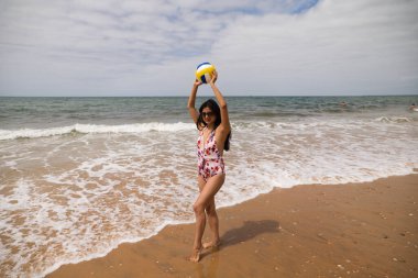 beautiful young woman playing beach volleyball on the seashore. The girl enjoys her holidays on a beach in Spain. Holiday and health concept.