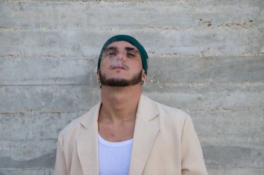 Sigara içen bej takım elbiseli ve yeşil başörtüsü takmış gri duvar arkaplanı olan genç bir adamın portresi. 31 Mayıs Dünya Günü sigaraya karşı. Toplumsal sorunu kabul et.