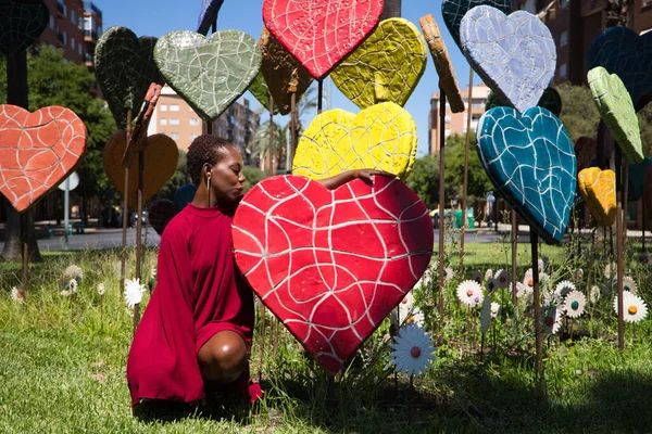 Young and beautiful Afro American woman hugging hearts of different sizes and colors in a park. Valentine's Day