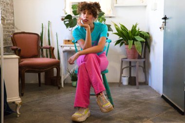 Parlak renkler giymiş genç ve güzel Latin kadın, moda tasarımının sandalyesinde oturuyor ve kameraya poz veriyor ve farklı pozlar ve ifadeler veriyor. kadın gücü