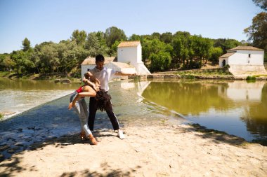 Güzel kadın ve yakışıklı erkek latin dansçıları ormanda nehrin kenarında dans ediyorlar. Çift dans ederken farklı pozlar verir. Dans konsepti ve ifadeleri.