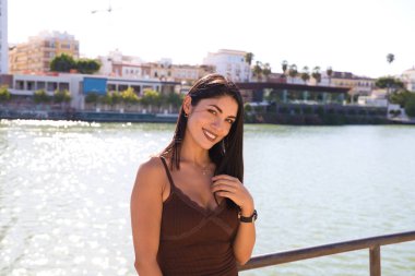 Güney Amerika 'dan genç ve güzel bir kadın ve kısa elbiseli, Seville' de tatilde. Arka planda nehir var. Kadın gülümser ve farklı ifadeler kullanır. Seyahat ve tatil.