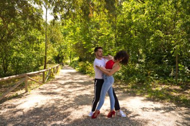 Yakışıklı genç adam ve kadın parkta bachata ve salsa dansı yapıyor. Çift, yeşilliklerle çevrili tutkuyla dans ediyor. Dans konsepti.