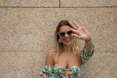Young beautiful blonde woman with sunglasses leaning against a brown wall in different postures and gestures, happy, sad, depressed, hateful, tired. Concept expressions