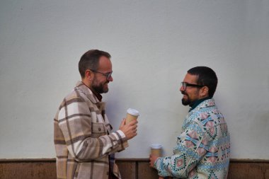 Genç bir çift eşcinsel sokakta geri dönüştürülmüş kağıt bardakta kahve içiyor. Çift gülüyor ve birbirlerine mutlu bir şekilde bakıyorlar..