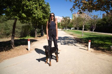 Güzel ve esmer İspanyol kadın bir Doberman köpeği olan köpeğini gezdiriyor. Kadın çok zarif siyah giyinmiş. Evcil hayvanlar ve hayvanlar konsepti.