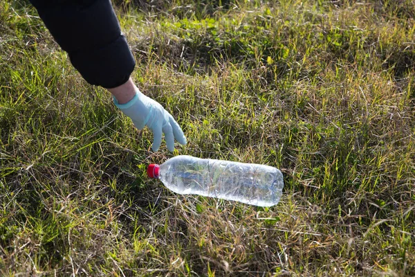 Detail of a volunteer\'s hand collecting plastic bottle from the forest. Concept of Earth Day and World Environment Day June 5.