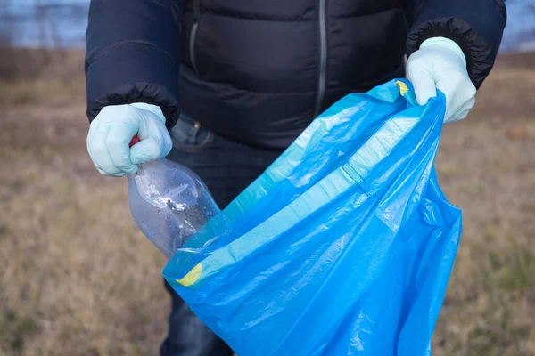 Detail of a volunteer\'s hand picking up plastic bottle from the forest and putting in the plastic bag. Concept of Earth Day and World Environment Day June 5.