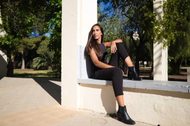 Parkta oturan güzel, koyu renk saçlı İspanyol kadın. Kadın düşünceli ve üzgün hiçbir yere bakmıyor ve siyah giyinmiş..