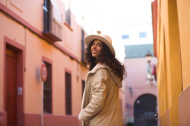 Young and beautiful Hispanic brunette woman with curly hair wearing a hat and coat for the cold walking in the city of seville while making different expressions and having fun.