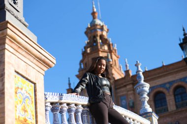 young and beautiful black latina woman is on holiday and visits the most important square in the city of Seville. The woman is dressed in black and she is leaning on the railing of the famous square.