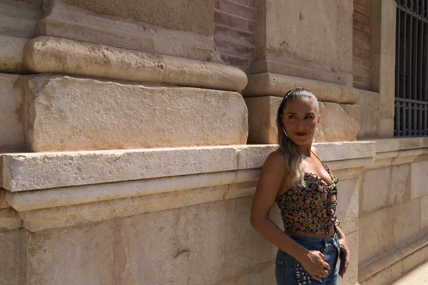 美しい若いブロンドのスペイン人女性はセビリアの古い建物の壁にもたれています 女性はジーンズをはいている 女性は観光とスペイン訪問です — ストック写真