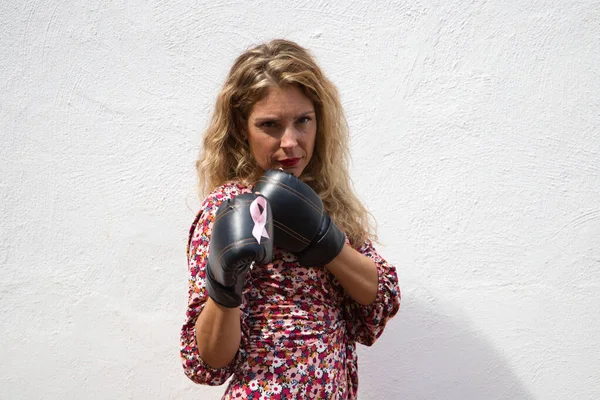 Young beautiful woman with boxing gloves with pink ribbon against breast cancer and white top on white background. Concept claims and world day against cancer.