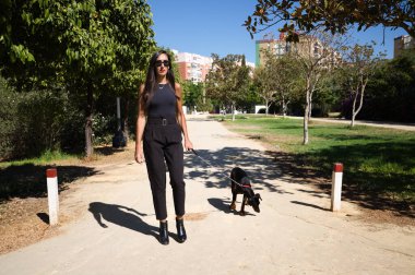 Güzel ve esmer İspanyol kadın bir Doberman köpeği olan köpeğini gezdiriyor. Kadın çok zarif siyah giyinmiş. Evcil hayvanlar ve hayvanlar konsepti.