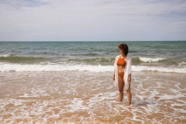 Sahilde yürüyen bikinili güzel bir kadın. Kadın farklı jestler ve ifadeler yaparken bir cennet kumsalına yolculuğunun tadını çıkarıyor..